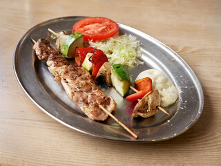 Grilled meat skewers with fresh vegetables and side salads served on a platter at a casual dining setting
