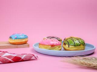 Colorful assorted donuts with icing and sprinkles on pastel pink background