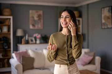 Fototapeta premium Smiling Brunette Woman Holding Phone in Bright Modern Living Room with Warm Natural Lighting