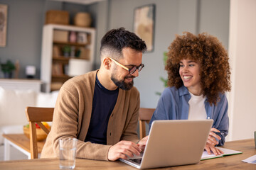 Obraz premium Mid-Aged Diverse Couple Collaborating On Project Using Laptop In Cozy Home Office With Natural Light