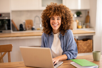 Smiling Woman with Curly Hair Working on Laptop at Wooden Table in Bright Modern Home