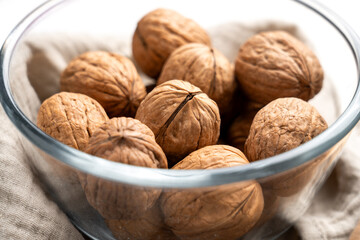 Whole raw walnuts with nutshells in glass bowl. Close-up. 