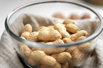 Roasted peanuts in glass bowl on crumpled cloth napkin close up