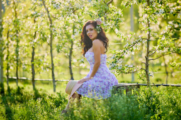 portrait of a beautiful woman in a dress sitting on a bench in a blooming apple orchard with a...