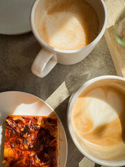 Close up of two cafe latte with heard design and a savory bun next to them on a plate, sunny and cozy