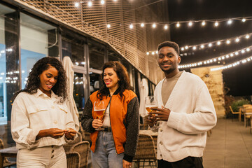 Multiethnic group of friends enjoying drinks and conversation at a rooftop party under string lights