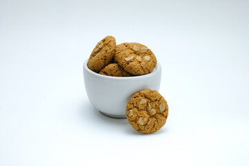 A round oatmeal cookies arranged inside and around a white ceramic cup, set against a plain white background. Ideal for use in healthy snack promotions, bakery packaging, recipe books
