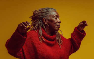 Naklejka na ściany i meble Portrait of a serene senior woman with gray dreadlocks, wearing a red turtleneck sweater against a vibrant yellow background, her hands gently outstretched. : Generative AI