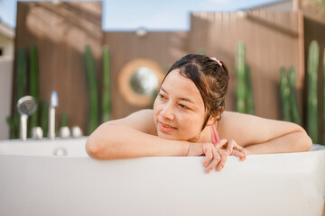 Attractive young woman feeling tired, leaning on bathtub side, bathing while relaxing at spa resort. Wellness, beauty and care concept 
