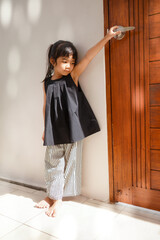 Asian girl child opens the big glass door of a cozy cafe. 
