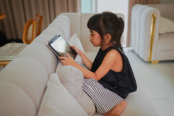 Child girl playing a game on tablet and sitting on sofa 

