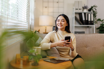 Fototapeta premium Happy hispanic teen girl holding cell phone using smartphone device at home. Smiling young asian woman blogger subscribing new social media, buying in internet, ordering products online in apps. 