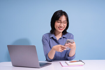 Young Asian woman engaging with smartphone at a desk in a modern workspace during daytime