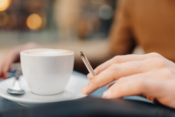Woman holding cigarette with cup of coffee in outdoor cafe