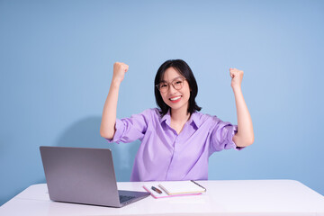Young Asian woman celebrates success at her workspace during daytime with a laptop and notebook