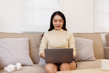 Fototapeta premium Beautiful Young Asian woman using laptop computer on sofa at home, shopping online with internet in happy mood and Relax part time concept 