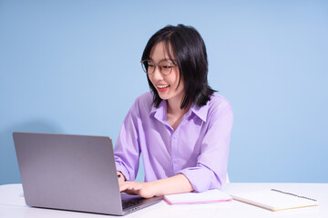 Young woman with glasses working on a laptop in a bright room, smiling while engaged in her task
