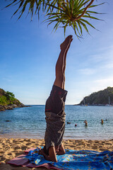 A man doing yoga in a headstand pose by the sea. Yanui Beach is a small, quiet beach with a small island in front of the clear blue water. It is a great place for snorkeling and relaxing.