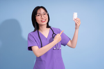 Smiling healthcare professional holding a medicine bottle while pointing, wearing scrubs with a...