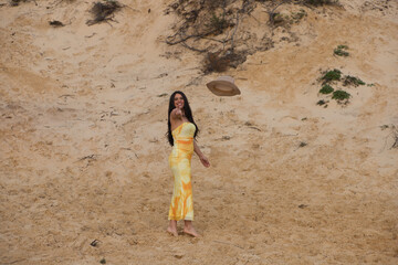 Young, beautiful brunette woman in a yellow dress is standing on the fine white sand between the...