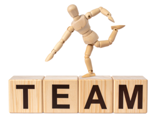 A wooden mannequin figure balances on wooden blocks spelling "TEAM" in bold black letters.