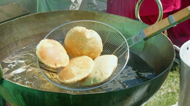 Punjabi puff bread, Poori, is scooped from large deep fry cauldron oil