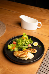 Grilled chicken paillard served with mustard sauce, arugula salad, California grapes, and mashed potatoes on a white plate, placed on a brown table in a restaurant setting