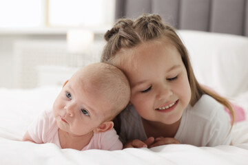 Cute girl and her little sister on bed at home