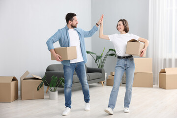 Moving day. Happy couple with cardboard boxes giving each other high five in their new home