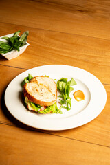 Classic vegetarian and cheese sandwich with a dip served on a white plate, placed on a brown table in a restaurant setting — a simple and satisfying café-style meal presentation.