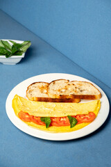Photo of a classic masala omelette served with fresh tomato slices, basil leaves, and bread on a white plate, set against a blue background in a Goan restaurant