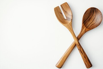 Hand-carved wooden salad servers with olive wood grain details, natural finish utensils crossed over white background, sustainable kitchenware product staging.