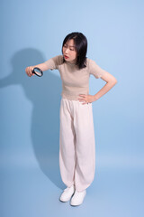 Young Asian woman exploring details with a magnifying glass against a light blue backdrop...