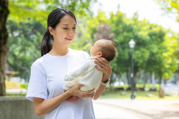 Happy mother holding newborn baby in green park
