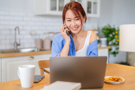 Asian adult Woman working from home in kitchen Beautiful young woman with an amputated arm working on a laptop and talking on a smartphone Woman Using Laptop At Home