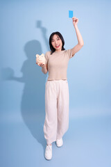 Young woman holding a piggy bank and a blue card, smiling joyfully against a light blue background