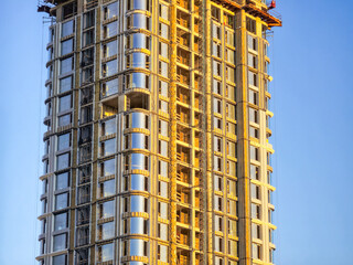 A tall building with a lot of windows and scaffolding. The building is under construction. The sky is blue and clear