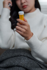 Fototapeta premium Sick young woman holding pill bottle at home