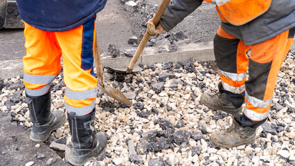 Two men in orange work clothes are shoveling gravel. Scene is hard work and determination