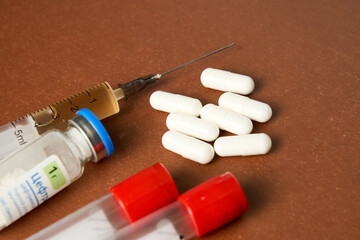 A syringe and pill bottle are on a table. The syringe is yellow and has a needle. The pill bottle...