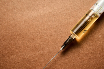 A syringe with a yellow liquid in it is on a brown surface. The syringe is partially filled with...