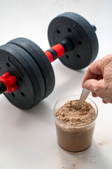 Hand Mixing Protein Powder Beside Dumbbell on White Surface