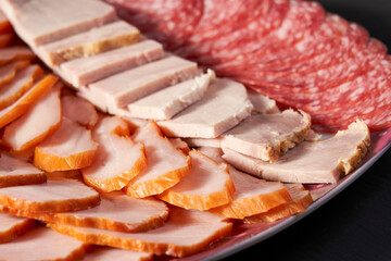 A plate of sliced meats and cheeses, including ham, turkey, and salami. The plate is arranged in a way that makes it easy to see the different types of meat and cheese. Scene is casual and inviting