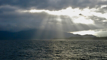 The sun's rays pass through the clouds over the sea. Gradient of sun rays. The sun's rays break through the storm clouds and illuminate the surface of the calm sea.
