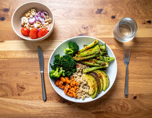 vegan meal featuring variety of colorful vegetables, including broccoli, asparagus, and sweet potatoes, served with quinoa and avocado. meal is presented wooden table alongside bowl