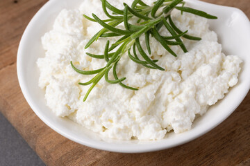 Creamy cottage cheese with fresh rosemary on a wooden tabletop