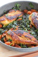 delicious cooked chicken breast with spinach and cherry tomatoes in a pan