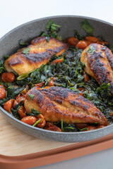 delicious cooked chicken breast with spinach and cherry tomatoes in a pan