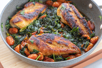 delicious cooked chicken breast with spinach and cherry tomatoes in a pan
