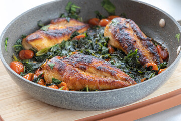 delicious cooked chicken breast with spinach and cherry tomatoes in a pan